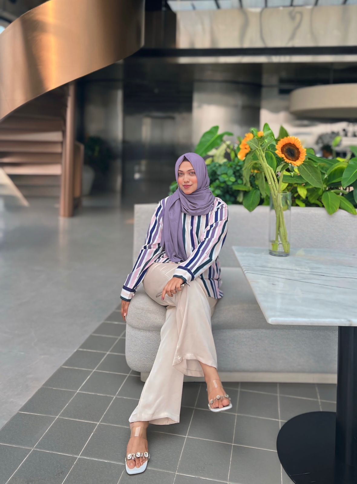 Sabrina in a lilac hijab and striped shirt in a modern architectural interior with sunflowers